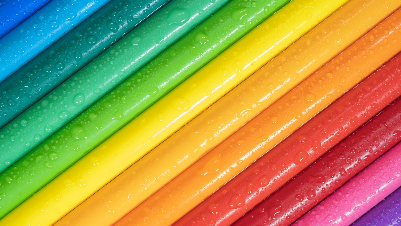 Brightly colored pencils with water droplets create a vibrant, rainbow-like appearance.